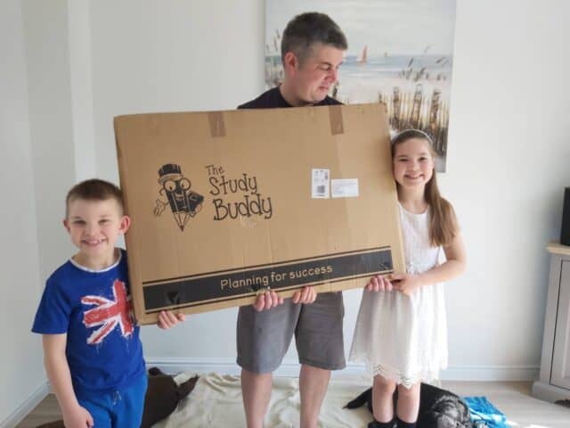 Growing children holding a large Study Buddy box, with one child and an adult smiling, highlighting the website's focus on educational tools and planning for success.