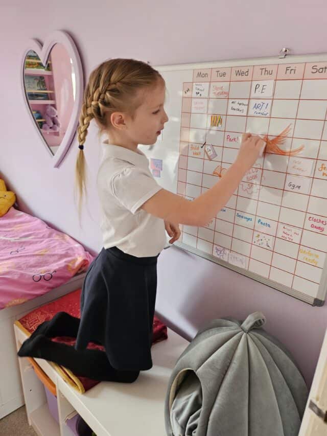 Study girl writing on a whiteboard calendar at home, showcasing the study buddy website for organising and planning educational activities for children.