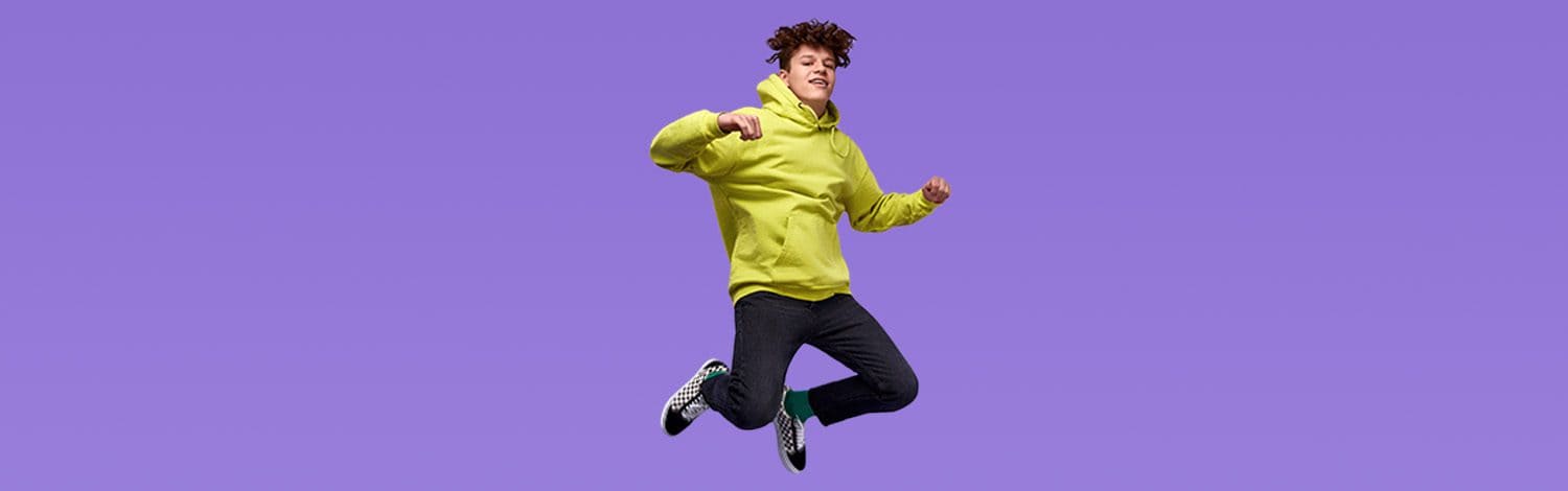 Jumping young man in a yellow hoodie on purple background, representing The Study Buddy website's focus on youth education and support.