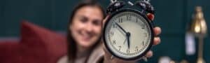 Alarm clock showing time, bright smile woman holds clock, The Study Buddy website focus, promoting effective study and time management tools, educational resource for students.