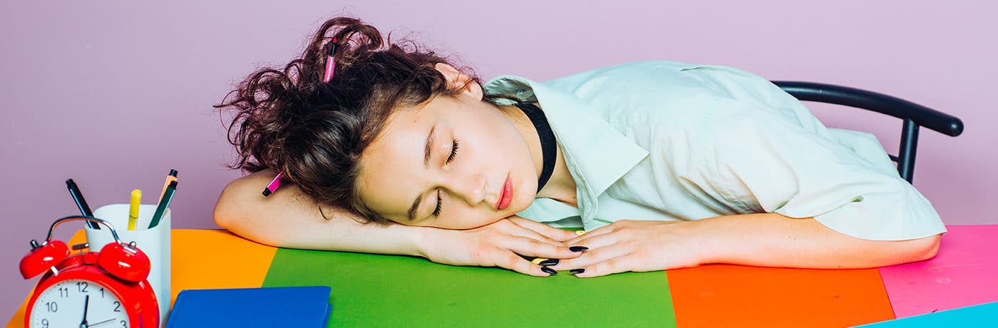 Sleepy student resting on colourful study table, representing stress relief solutions from The Study Buddy website.