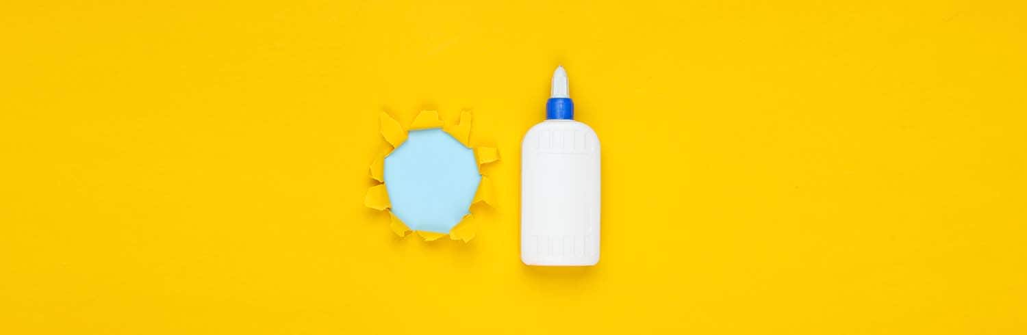 - Bottle of glue and torn paper with blue background on yellow surface.