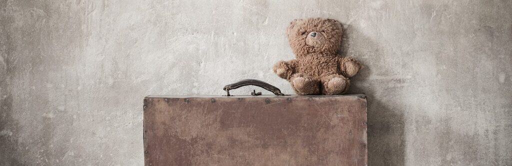 Teddy bear sitting on vintage suitcase against textured wall, nostalgic childhood toy, The Study Buddy website focus on educational support, comforting and friendly learning environment.