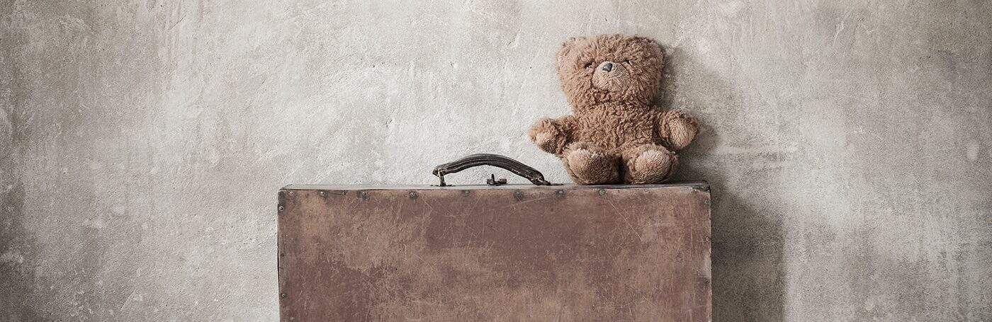 Teddy bear sitting on vintage suitcase against textured wall, nostalgic childhood toy, The Study Buddy website focus on educational support, comforting and friendly learning environment.