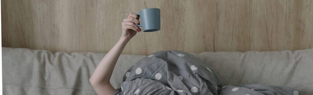 Relaxed person lounging on a beige sofa with a blanket, holding a blue mug in a comfortable home setting, representing the user-friendly and supportive environment of The Study Buddy website.