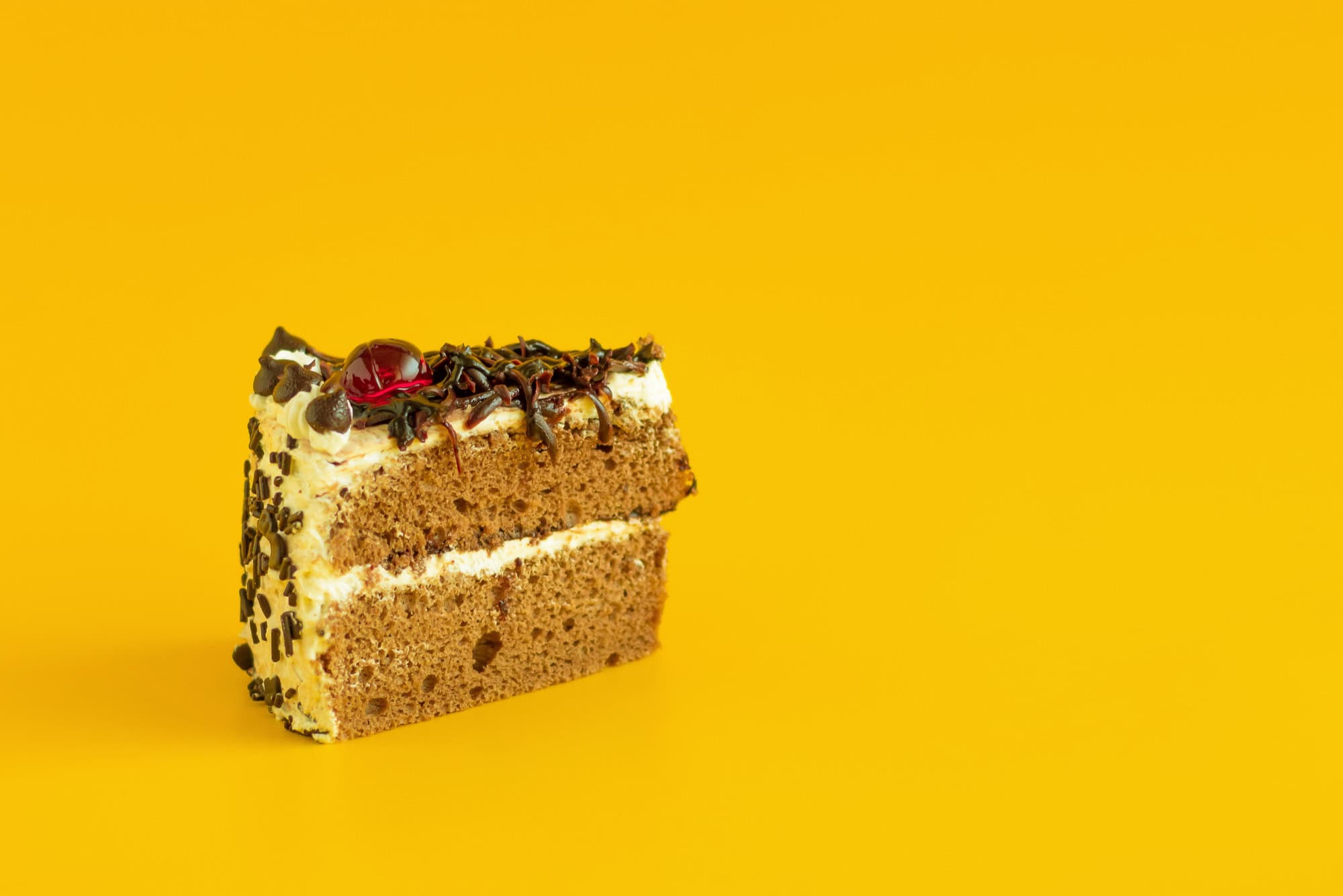 Chocolate and vanilla layered cake slice with sprinkles and cherry on top against a bright yellow background, showcasing The Study Buddy website's focus on engaging and colourful educational content.