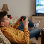 An image of a teen playing video games, lounging about. Not studying.